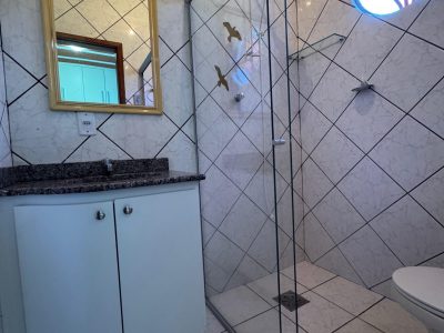 Quarto de casal simples e organizado com cama arrumada e armários brancos, seguido de banheiro privativo (suíte) com box de vidro e bancada em granito no Recanto do Bem.