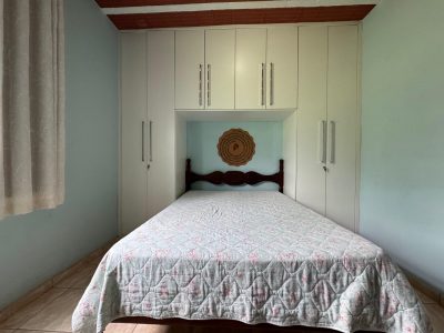 Quarto de casal simples e organizado com cama arrumada e armários brancos, seguido de banheiro privativo (suíte) com box de vidro e bancada em granito no Recanto do Bem.