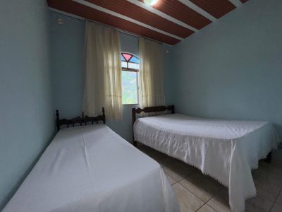 Quarto de solteiro com duas camas individuais, colchas brancas impecáveis e janela com cortina clara, revelando ambiente arejado e higienizado no Recanto do Bem.