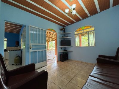 Sala de estar e TV com sofás de couro marrom, paredes azuis claras e vista para a varanda e cozinha integrada na casa de campo Recanto do Bem em Moeda.